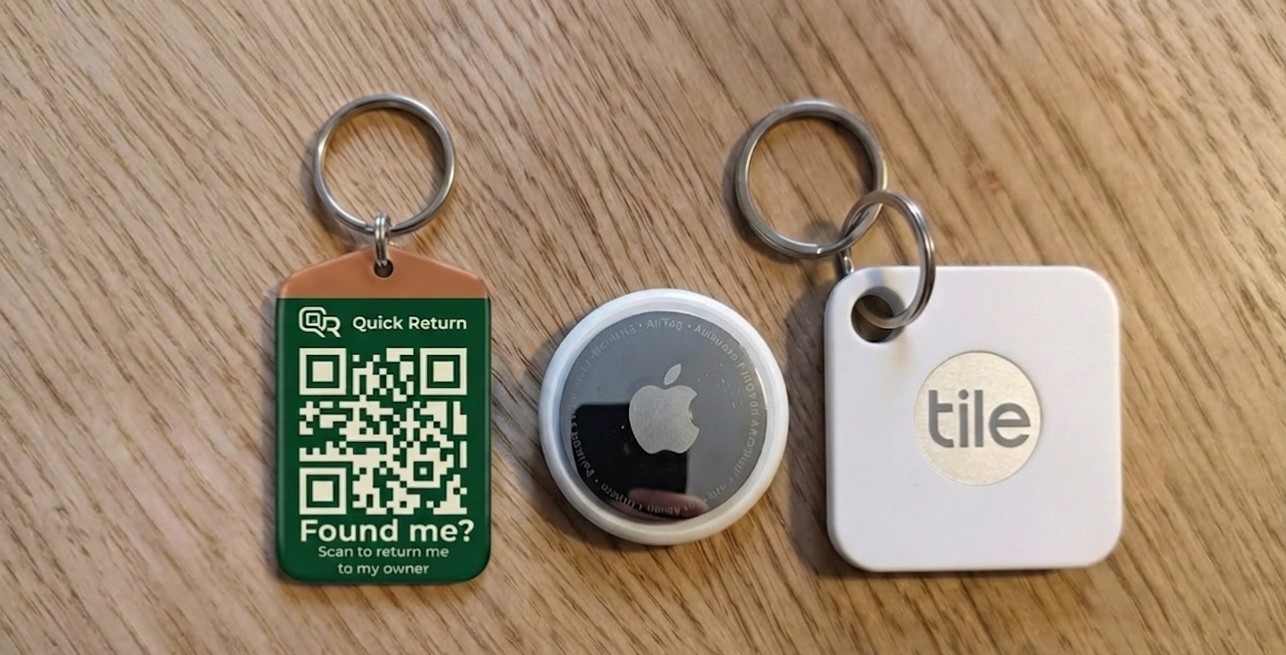 A QR keyring beside an Apple AirTag and a Tile Mate on a wooden table